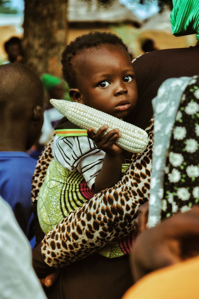 gallery-4 A child holds corn in a colorful outdoor setting in Nalerigu, Ghana.